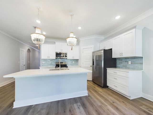 kitchen with appliances with stainless steel finishes, decorative light fixtures, sink, white cabinets, and a kitchen island with sink