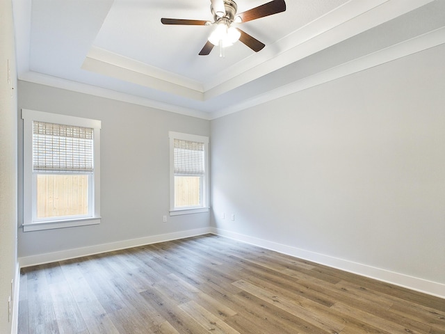 spare room featuring crown molding, a tray ceiling, wood finished floors, and baseboards