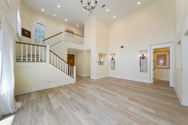 unfurnished living room featuring light wood-type flooring, an inviting chandelier, and a towering ceiling