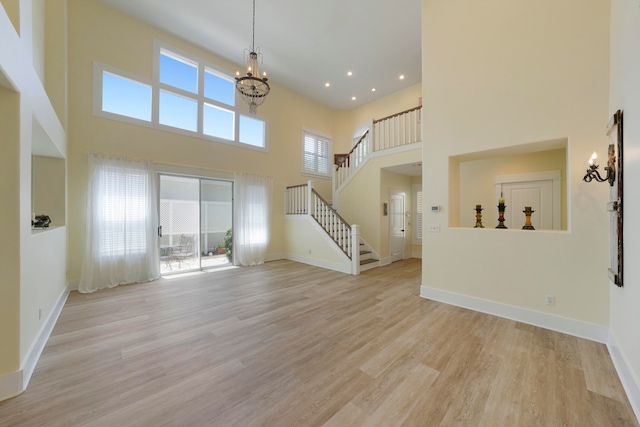 unfurnished living room with light hardwood / wood-style floors, a healthy amount of sunlight, and a towering ceiling