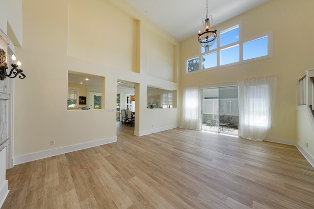 unfurnished living room with light hardwood / wood-style floors, a high ceiling, a healthy amount of sunlight, and a notable chandelier