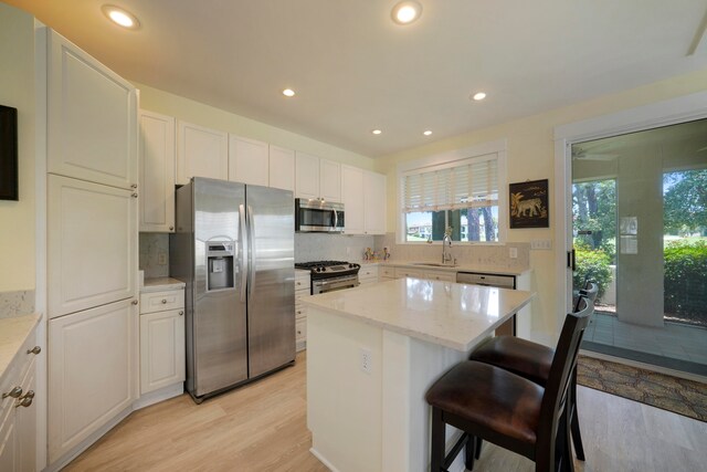 kitchen with a kitchen island, light wood-type flooring, appliances with stainless steel finishes, light stone countertops, and sink