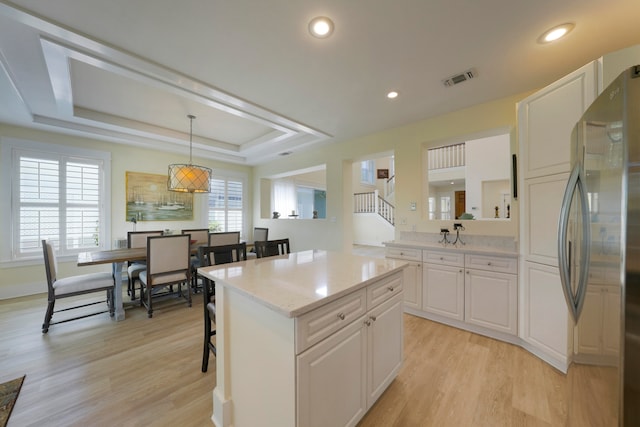 kitchen with light hardwood / wood-style floors, white cabinets, hanging light fixtures, a kitchen island, and stainless steel fridge