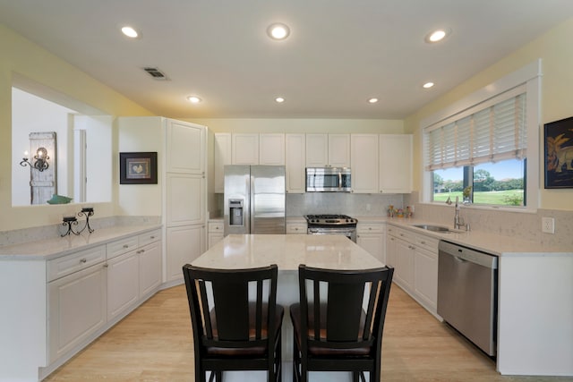 kitchen featuring stainless steel appliances, light hardwood / wood-style floors, white cabinetry, sink, and a center island