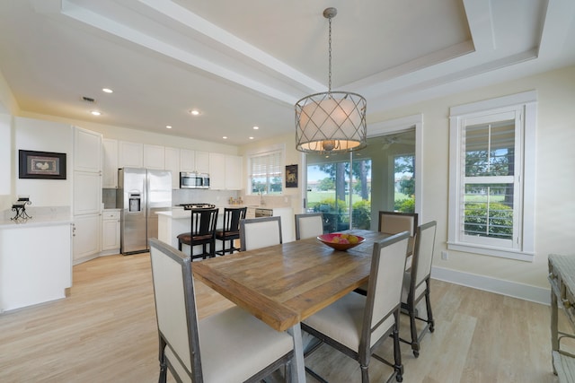 dining area with light hardwood / wood-style floors and a tray ceiling