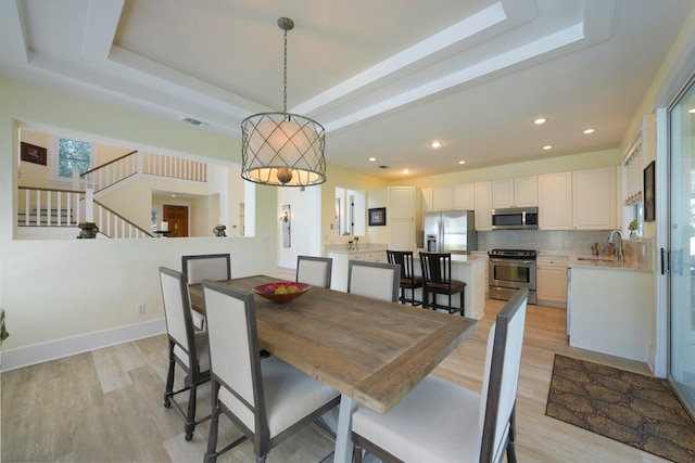 dining room with light hardwood / wood-style flooring, sink, and a raised ceiling