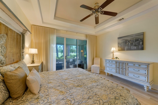 bedroom with ceiling fan, access to exterior, light wood-type flooring, and a tray ceiling