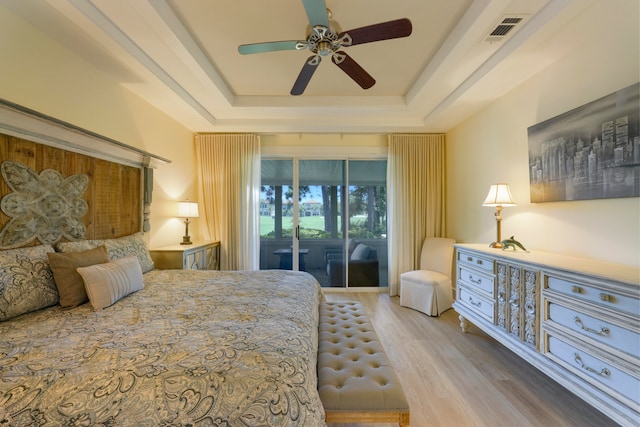 bedroom featuring access to outside, hardwood / wood-style floors, ceiling fan, and a raised ceiling