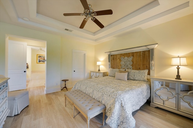 bedroom with light hardwood / wood-style floors, ceiling fan, and a raised ceiling