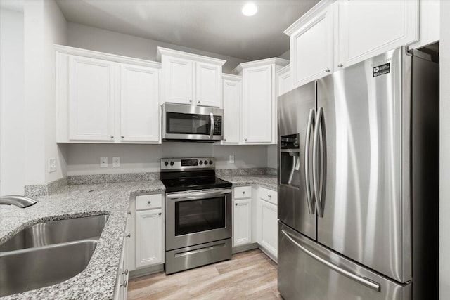 kitchen with sink, white cabinetry, light stone counters, appliances with stainless steel finishes, and light hardwood / wood-style floors