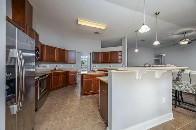 kitchen featuring a kitchen island with sink, hanging light fixtures, ceiling fan, a kitchen bar, and stainless steel appliances