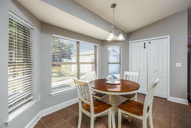 dining room featuring an inviting chandelier, dark tile patterned flooring, and lofted ceiling