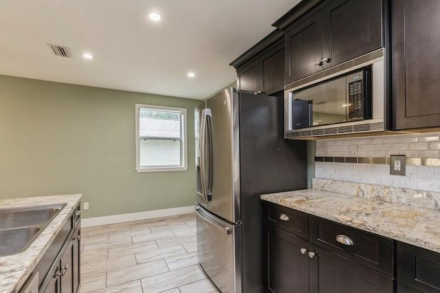 kitchen with sink, decorative backsplash, light stone countertops, built in microwave, and stainless steel refrigerator