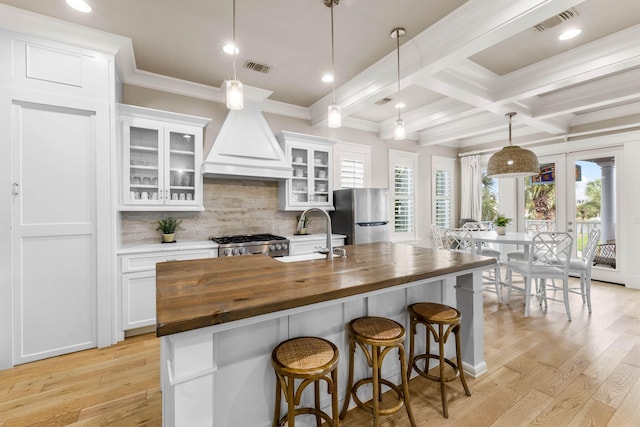 kitchen featuring wood counters, appliances with stainless steel finishes, sink, a center island with sink, and white cabinetry