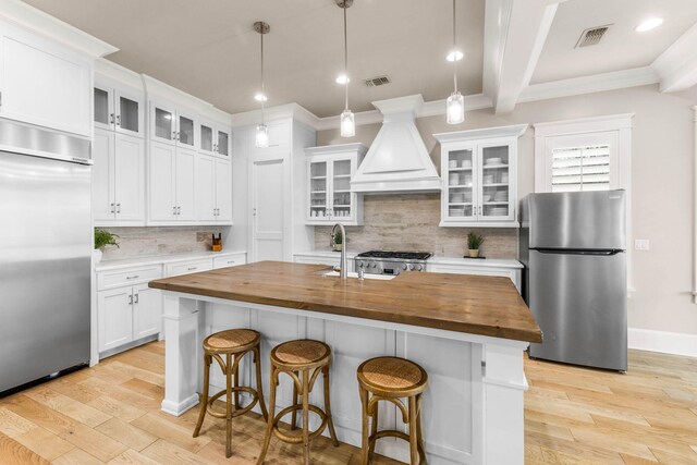 kitchen with white cabinets, wood counters, stainless steel appliances, and a kitchen island with sink