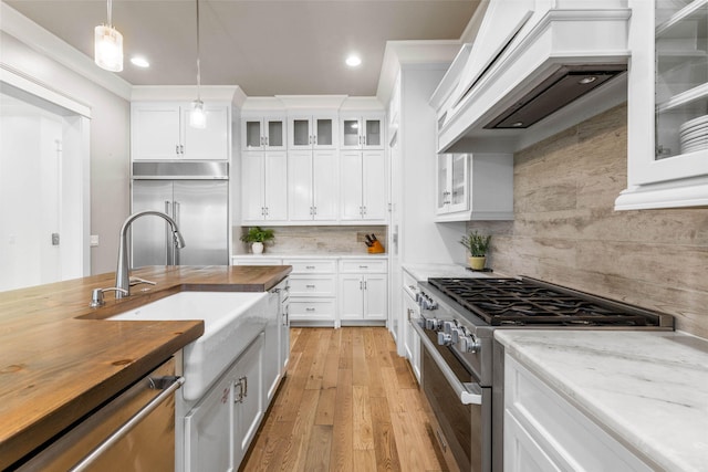 kitchen featuring high quality appliances, white cabinetry, premium range hood, and wooden counters