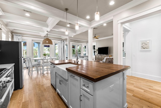 kitchen with butcher block countertops, pendant lighting, light hardwood / wood-style floors, a kitchen island with sink, and appliances with stainless steel finishes