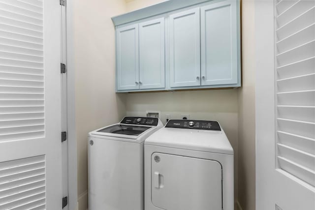 clothes washing area with washing machine and clothes dryer and cabinets