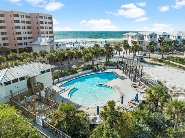 view of swimming pool with a patio area, a water view, and a view of the beach