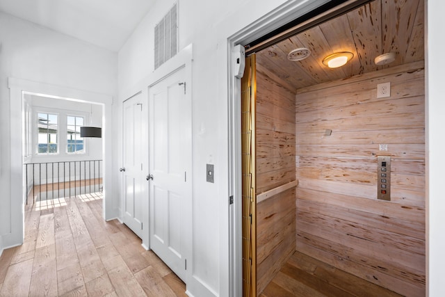 hallway featuring wooden walls, wood ceiling, and light wood-type flooring