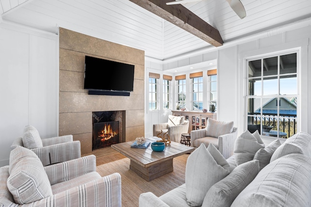 living room featuring beam ceiling, a wealth of natural light, a fireplace, and light hardwood / wood-style flooring