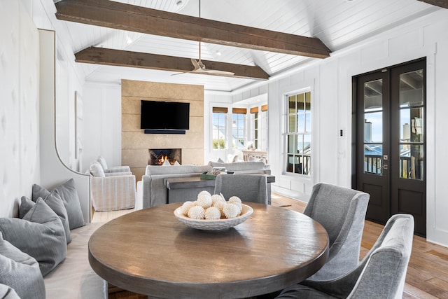 dining room with light wood-type flooring, lofted ceiling with beams, ceiling fan, and a fireplace