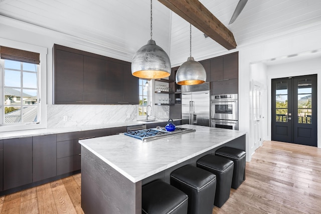 kitchen featuring light wood-type flooring, tasteful backsplash, stainless steel appliances, decorative light fixtures, and a center island