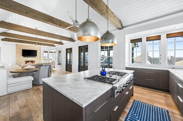 kitchen with stainless steel gas cooktop, pendant lighting, beam ceiling, light hardwood / wood-style flooring, and a large island