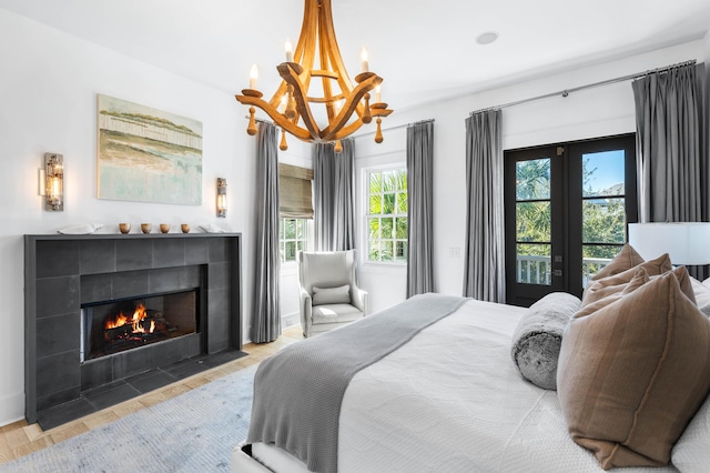 bedroom with access to exterior, light hardwood / wood-style flooring, a tiled fireplace, and an inviting chandelier