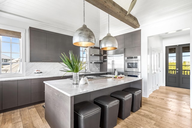 kitchen featuring tasteful backsplash, light hardwood / wood-style floors, decorative light fixtures, a kitchen island, and appliances with stainless steel finishes