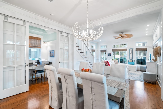 dining room with hardwood / wood-style floors, ceiling fan with notable chandelier, a wealth of natural light, and crown molding