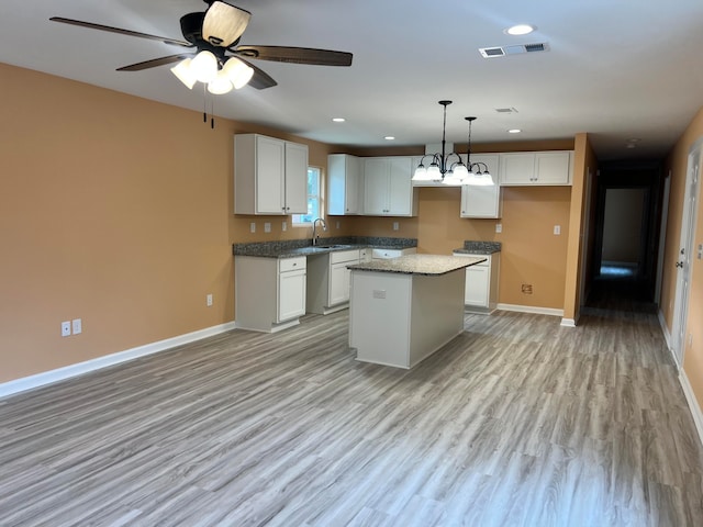 kitchen with a center island, white cabinetry, stone countertops, sink, and light hardwood / wood-style flooring