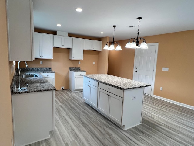 kitchen featuring light wood-type flooring, hanging light fixtures, sink, white cabinets, and a center island
