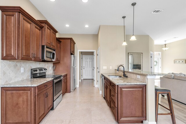 kitchen featuring stainless steel appliances, a breakfast bar, kitchen peninsula, light stone counters, and decorative light fixtures