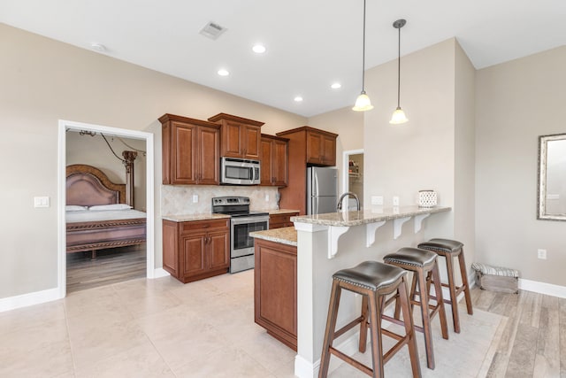 kitchen featuring light stone counters, backsplash, appliances with stainless steel finishes, hanging light fixtures, and kitchen peninsula