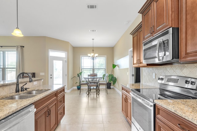 kitchen with hanging light fixtures, sink, light stone counters, and stainless steel appliances