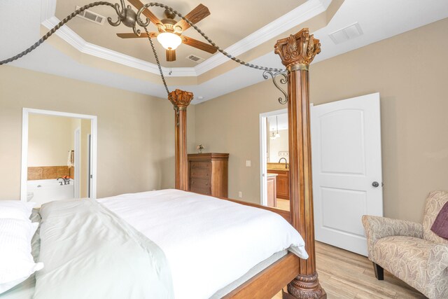 bedroom featuring light wood-type flooring, a raised ceiling, and connected bathroom