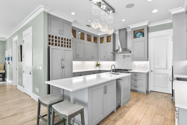 kitchen featuring wall chimney exhaust hood, a kitchen island with sink, paneled built in fridge, light hardwood / wood-style flooring, and crown molding