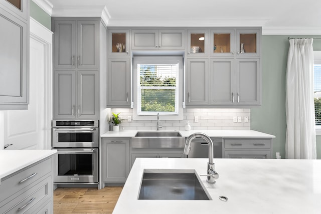 kitchen with decorative backsplash, light wood-type flooring, sink, and double oven