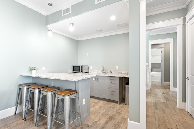 kitchen with light hardwood / wood-style floors, a kitchen breakfast bar, crown molding, gray cabinets, and pendant lighting