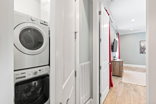 clothes washing area featuring light hardwood / wood-style flooring, crown molding, and stacked washer and clothes dryer