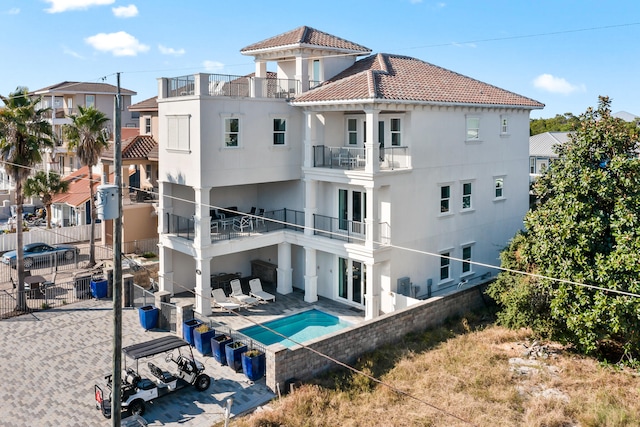 rear view of property featuring a patio, a balcony, and a fenced in pool