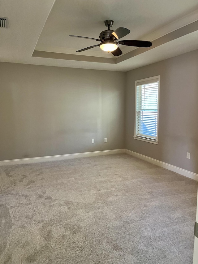 unfurnished room featuring a raised ceiling, light carpet, and ceiling fan