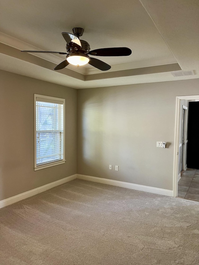 unfurnished room featuring a raised ceiling, light carpet, and ceiling fan