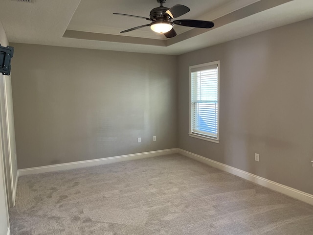 empty room featuring ceiling fan, a raised ceiling, and light carpet