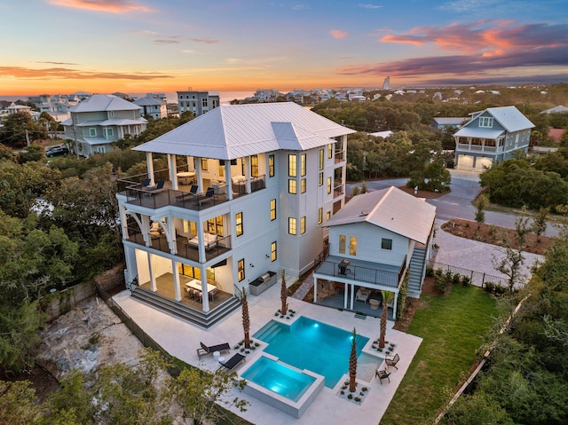 back house at dusk with outdoor lounge area, a patio, a balcony, and a swimming pool with hot tub