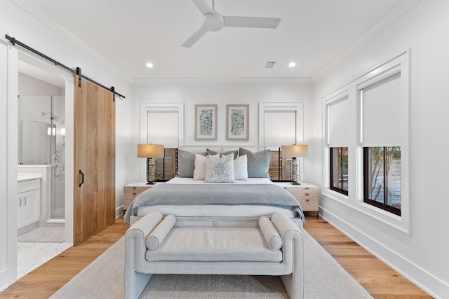 bedroom featuring ensuite bath, a barn door, ornamental molding, ceiling fan, and light hardwood / wood-style flooring