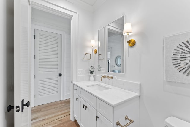 bathroom featuring toilet, vanity, wood-type flooring, and crown molding