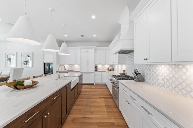 kitchen with high end stove, decorative light fixtures, sink, and white cabinets