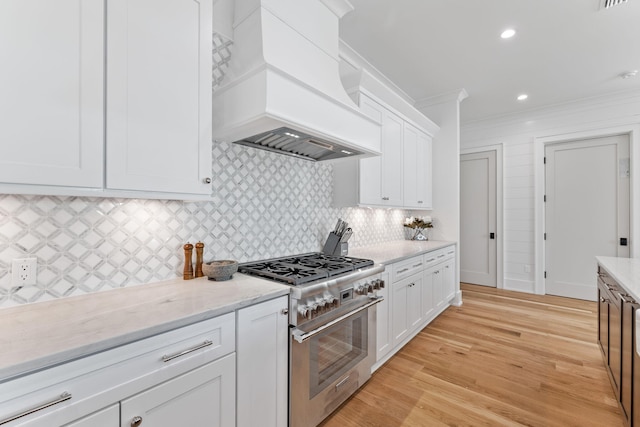 kitchen with ornamental molding, custom range hood, white cabinets, high end stainless steel range, and light wood-type flooring